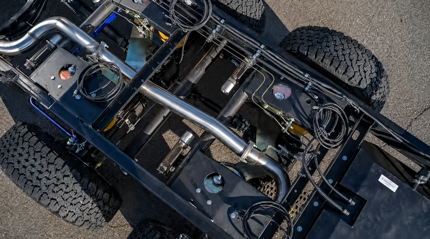Underside view of the JMACX 6x6 chassis showing the pass-through driveline, jackshaft and tandem rear axles